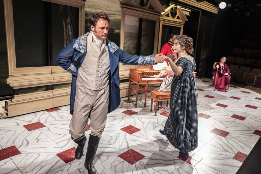 a man and a woman in regency dress dancing in a circle on a stage